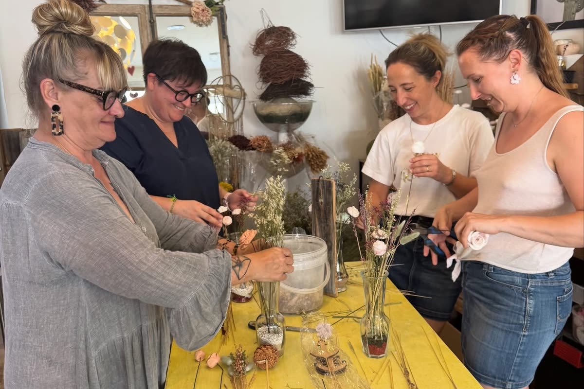 Quatre participantes composent leurs créations autour de la grande table jaune de la boutique, pendant un atelier