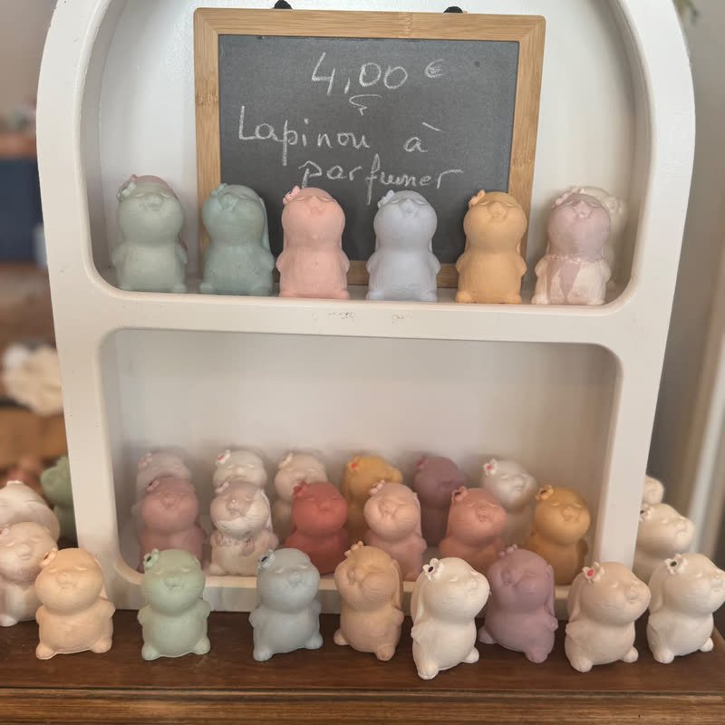 Petits lapins en gypse pastel à parfumer sur une étagère blanche, avec une ardoise indiquant 4 euros