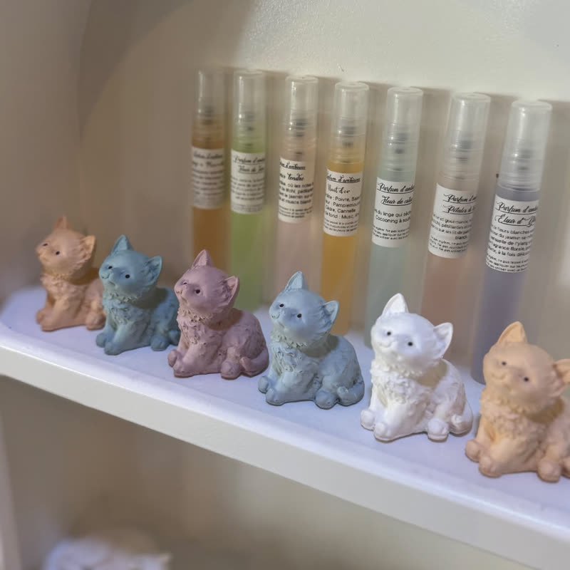 Petits chats en gypse pastel à parfumer, alignés devant les flacons de parfum d'ambiance de la boutique