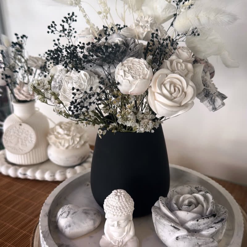 Bouquet de fleurs en gypse blanches et fleurs séchées noires dans un vase noir, sur un plateau blanc