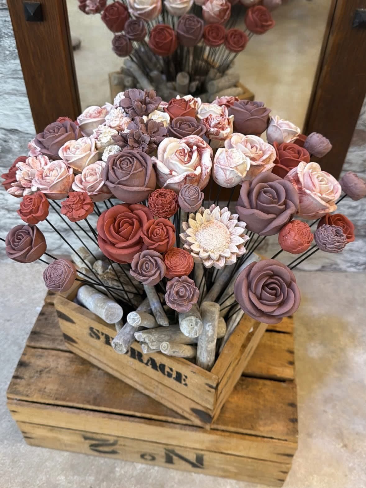 Roses et fleurs en gypse sur tiges dans une caisse en bois, devant le mur de pierre de la boutique